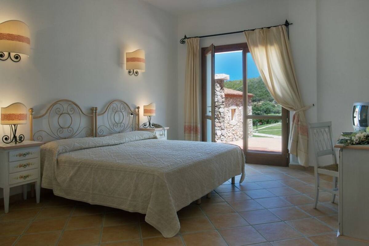 Ein Schlafzimmer mit Bett, Nachttischen, einem Schreibtisch mit Stuhl und Blick ins Freie.