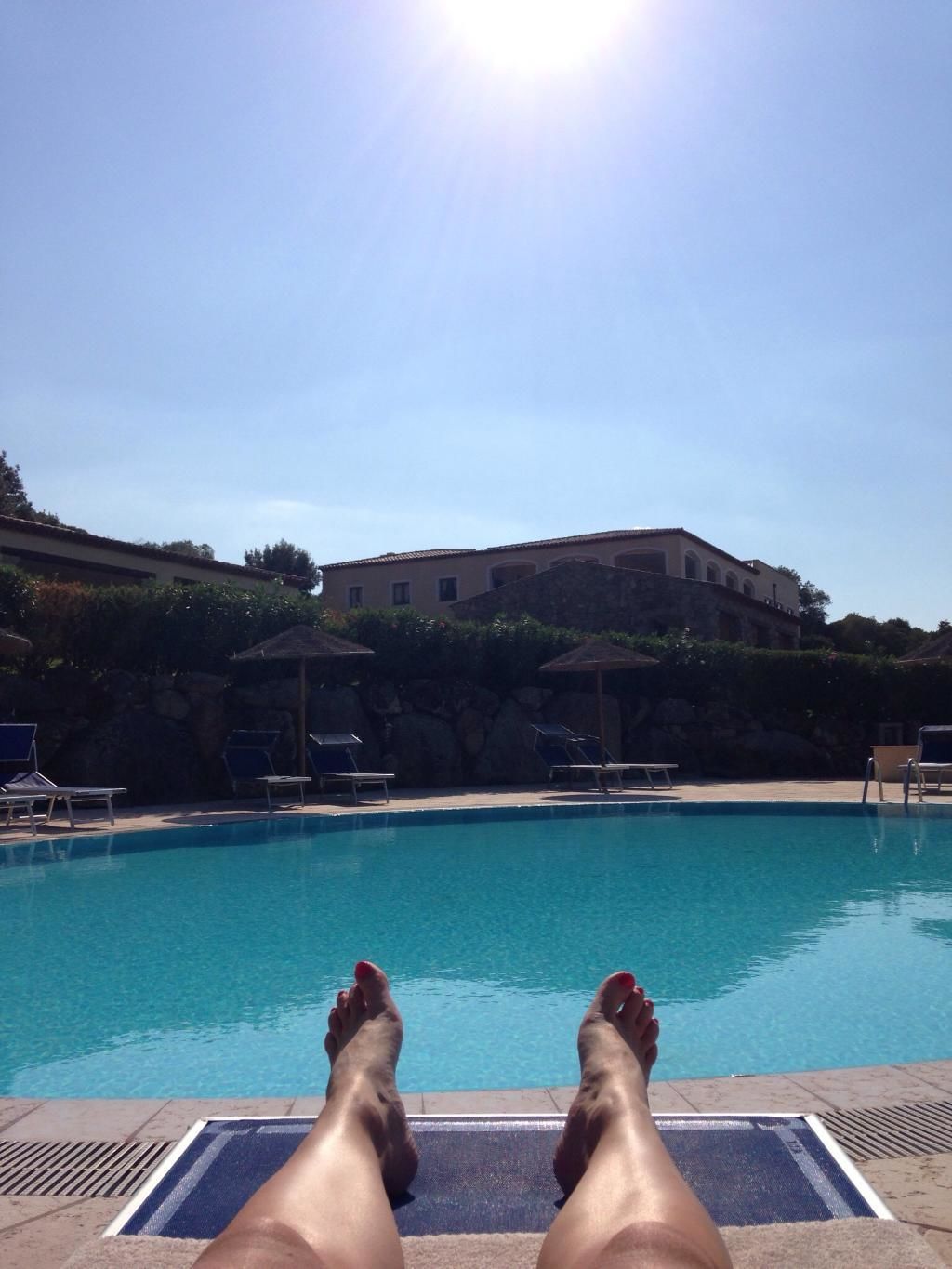 A poolside view with lounge chairs and a stone wall in the background.