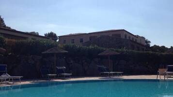 A poolside view with lounge chairs and a stone wall in the background.