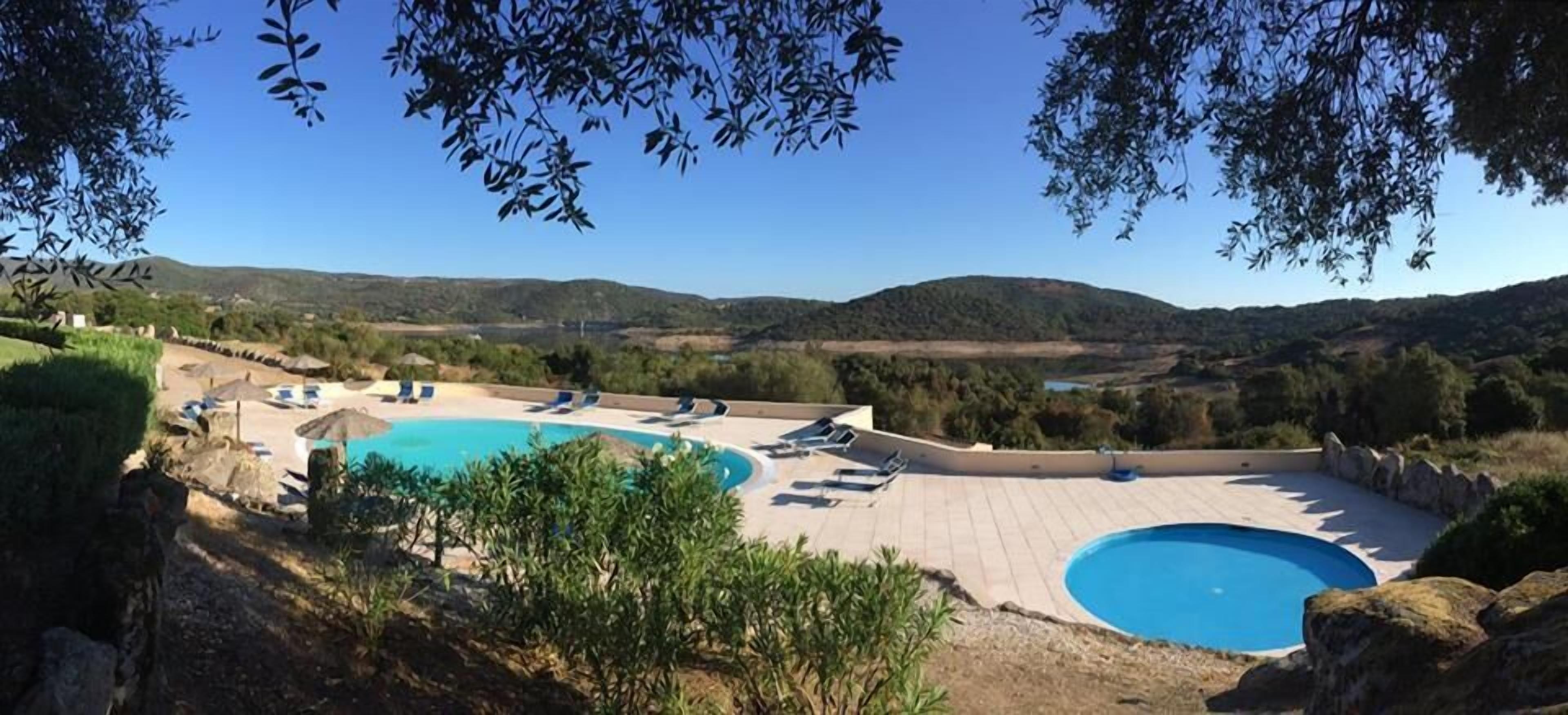 A pool area with two pools, sun loungers, and a view of the surrounding landscape.