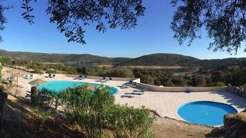 A pool area with two pools, sun loungers, and a view of the surrounding landscape.