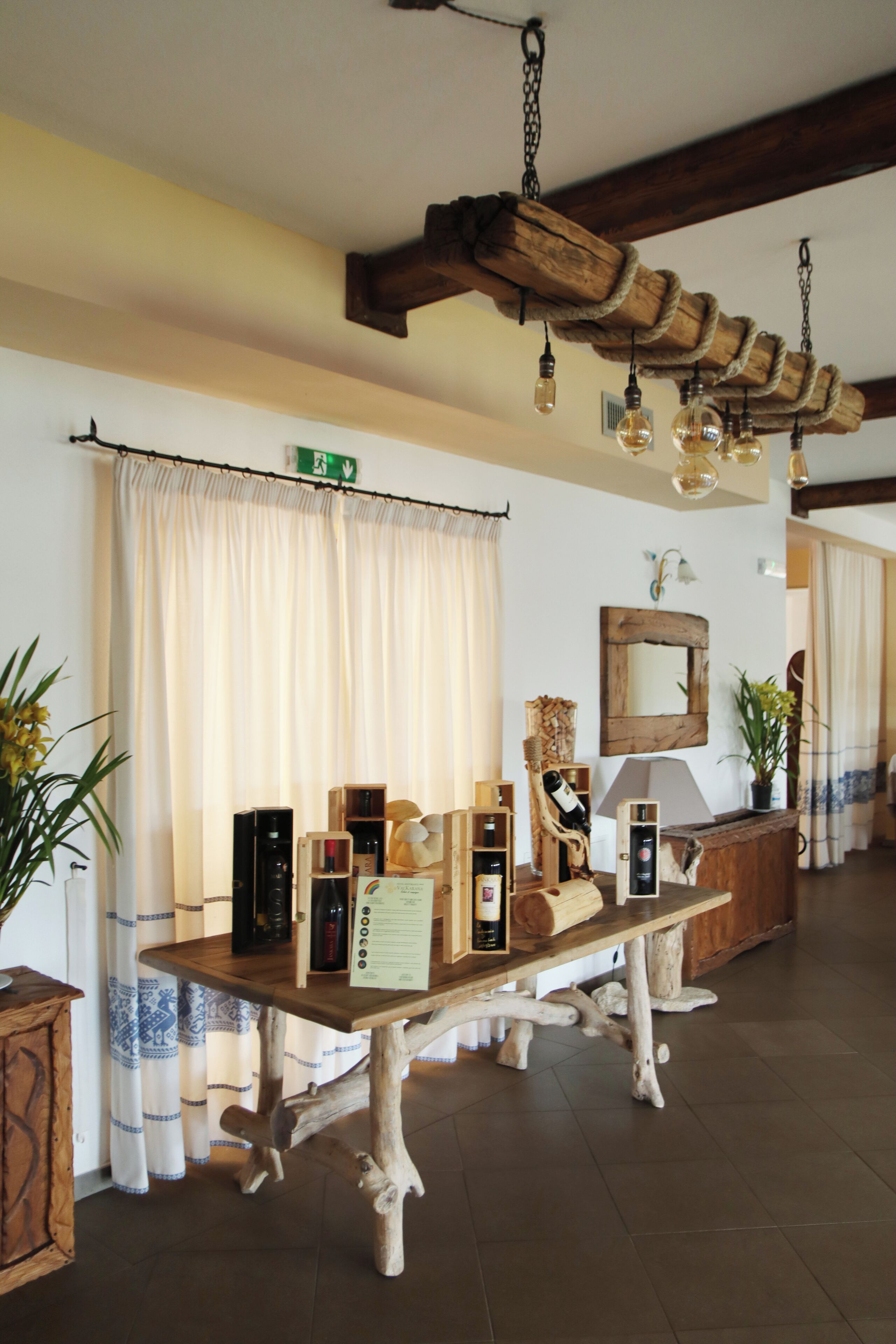 A wooden table with various items, a mirror, and a hanging light fixture in a room with curtains and a wooden ceiling.