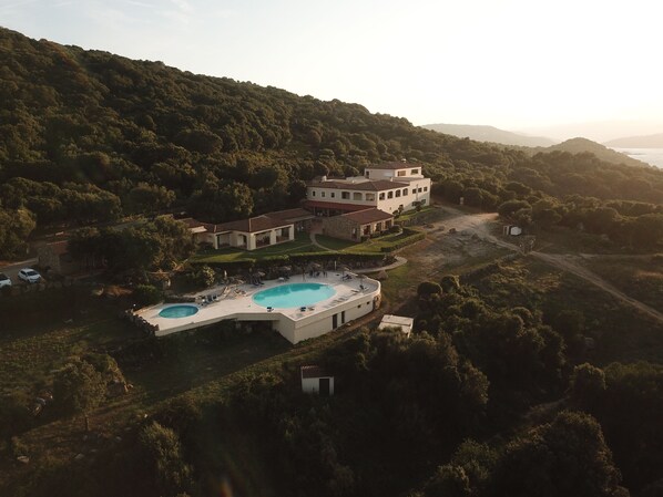 A large, modern villa with a swimming pool, surrounded by lush greenery and hills. - Hotel Relais Valkarana (Sant'Antonio di Gallura)