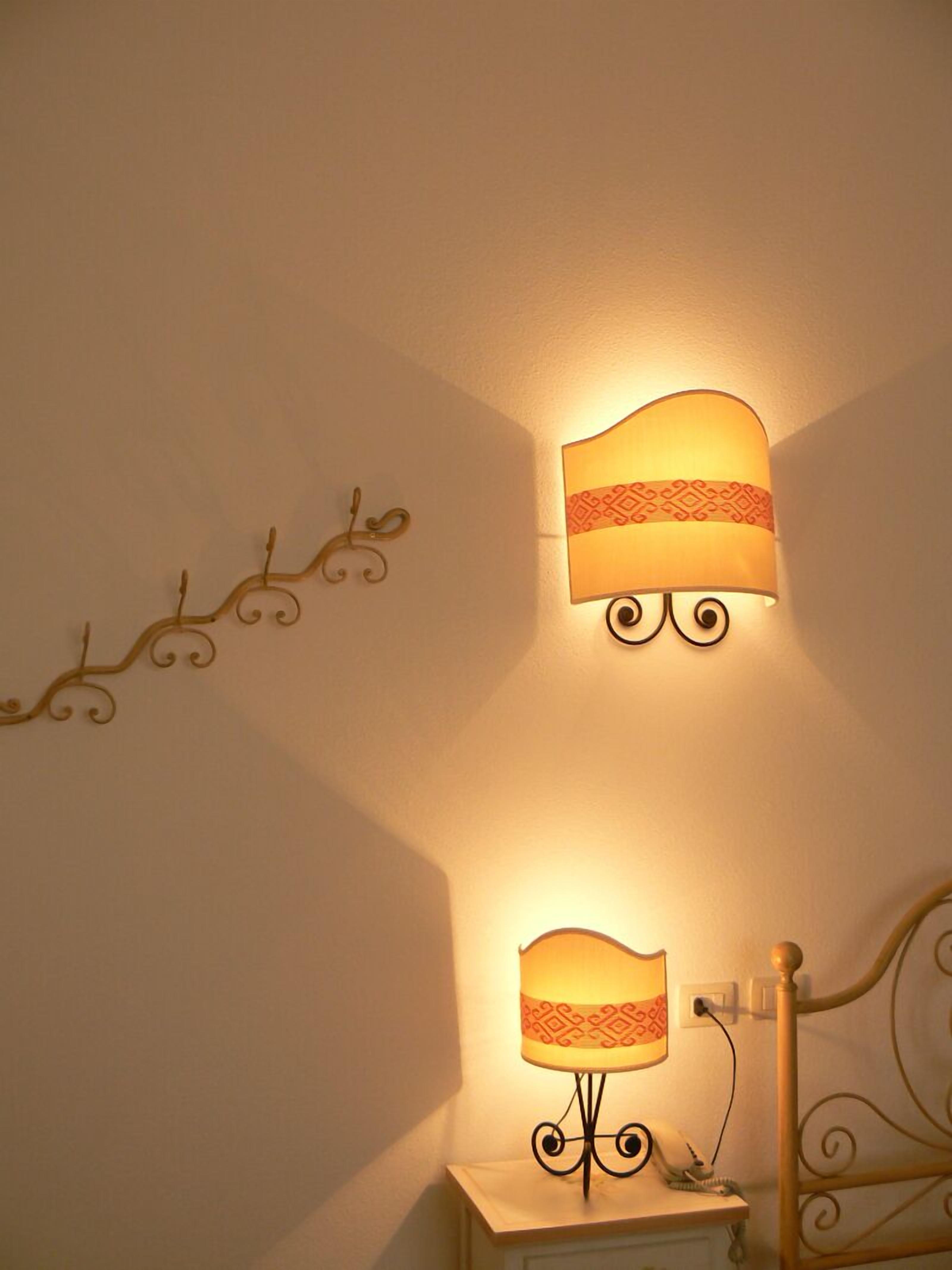 A wall-mounted lamp with a decorative design, a small bedside table with a lamp, and a metal headboard.