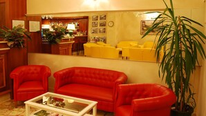 A living room with a red sofa set, a coffee table, and a large mirror reflecting the room. There is a bar area in the background with various items on display. - Eden (Salo)