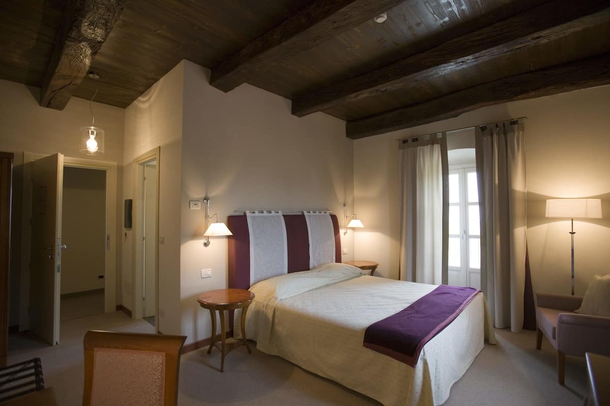 Ein Hotelzimmer mit einem Bett, zwei Nachttischlampen, einem Sessel und einem Fenster mit Vorhängen.