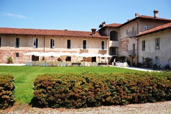A courtyard with a building featuring a tiled roof, multiple windows, and outdoor seating with umbrellas. - Antico Podere Propano (Saluzzo)