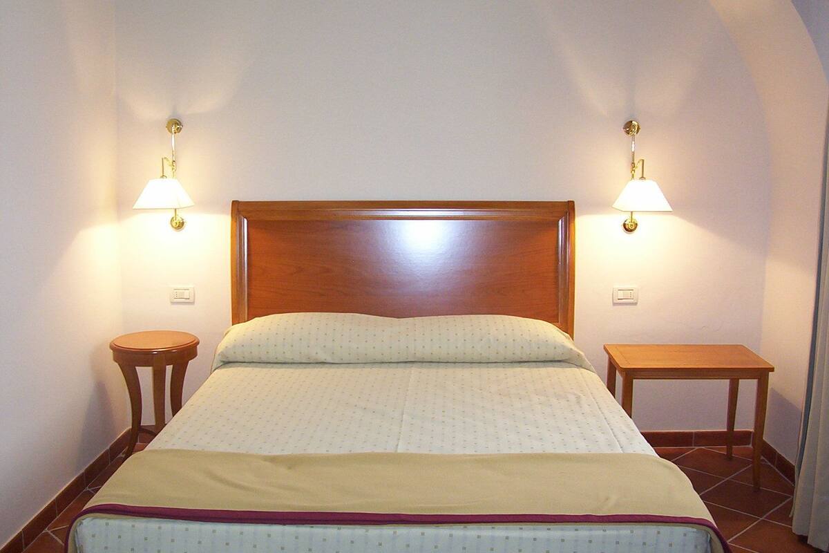 Ein ordentlich bezogenes Bett mit Holz-Kopfstück, zwei Nachttischen und Wandlampen.