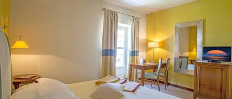 Una habitación de hotel con cama, escritorio, silla, televisor y espejo.