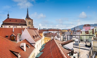 Paisagem urbana com telhados de telhas vermelhas, uma igreja imponente com torre de relógio e um edifício rosa ao longe.