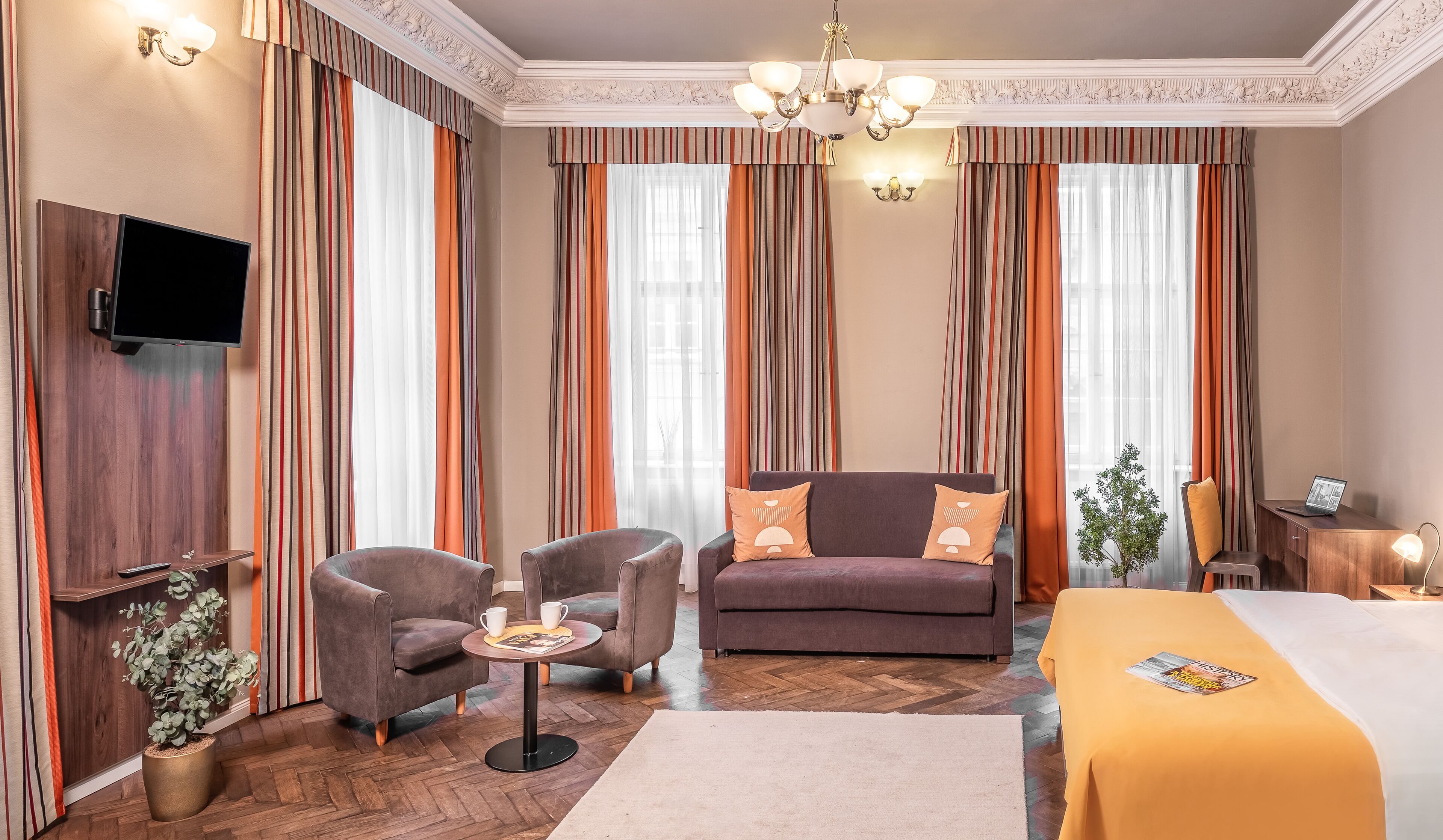 A hotel room with a sofa, two armchairs, a coffee table, a TV, a bed, and a desk with a lamp.