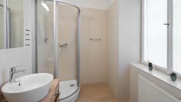 A modern bathroom with a curved glass shower, a white sink, and a window with potted plants.