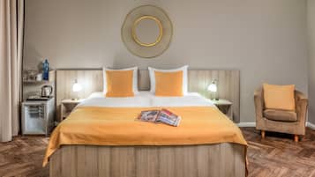 Une chambre d’hôtel avec une tête de lit en bois, un lit avec une literie blanche et orange, une table de chevet avec une lampe, une chaise et un miroir fixé au mur.