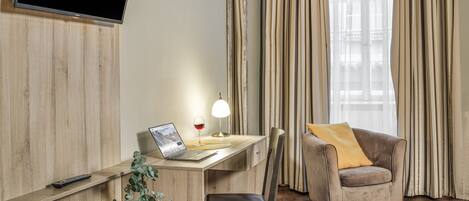 A modern room with a wooden desk, a laptop, a glass of red wine, a lamp, a chair, and a television mounted on the wall.