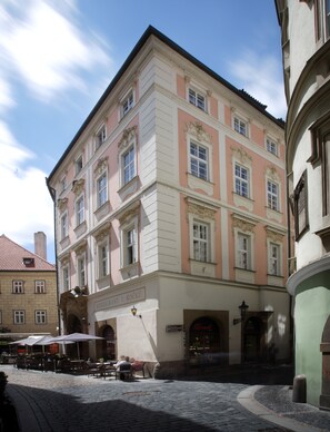 A historic building with a pink facade, multiple windows, and a ground-level entrance with outdoor seating. - Hotel Palác U Kočků by Adrez Living (Prague)