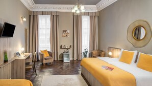A hotel room with a large bed, a desk with a laptop, a chair, a TV mounted on the wall, and a decorative mirror.
