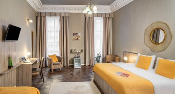 Quarto de hotel com uma cama grande, uma escrivaninha com um laptop, uma cadeira, uma televisão na parede e um espelho decorativo.