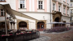 A historic building with a pink facade, large windows, and a covered outdoor seating area with tables and chairs. - Hotel Palác U Kočků by Adrez Living (Prague)