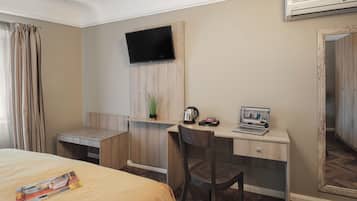 A hotel room with a bed, a desk with a laptop, a TV, and a mirror.