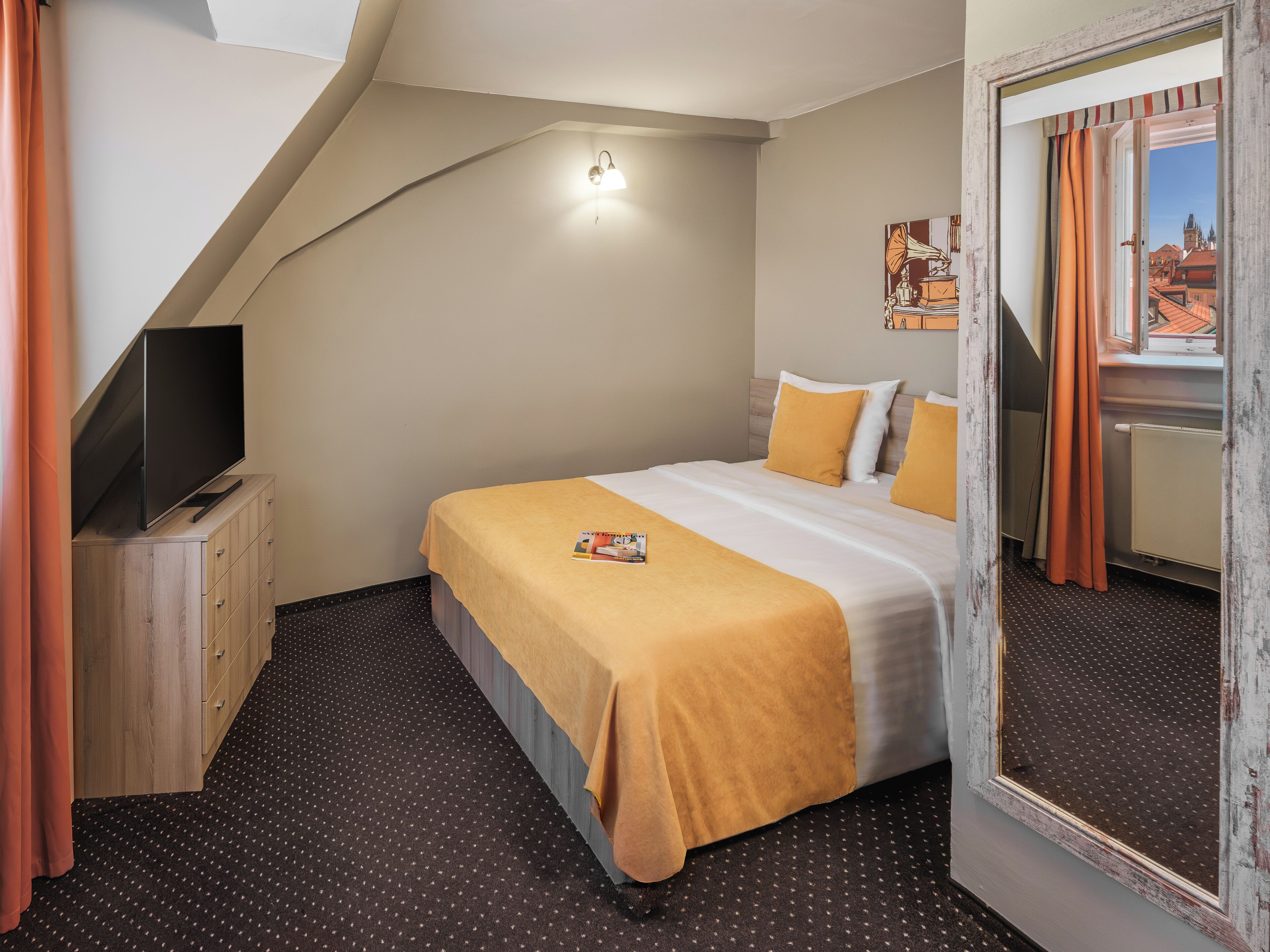 Ein Hotelzimmer mit einem Bett, einem Fernseher auf einer Holzkommode, einer Wandleuchte und einem großen Spiegel.