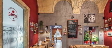 Interior de restaurante com mesas e cadeiras de madeira, parede vermelha e teto com vigas aparentes.