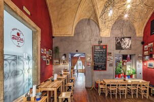 Interior de restaurante com mesas e cadeiras de madeira, parede vermelha e teto com vigas aparentes.