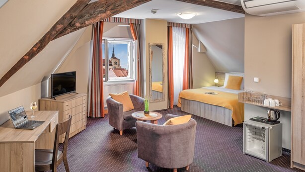 A cozy hotel room with a loft bed, a desk with a laptop, a chair, a small table with a vase, and a minibar.