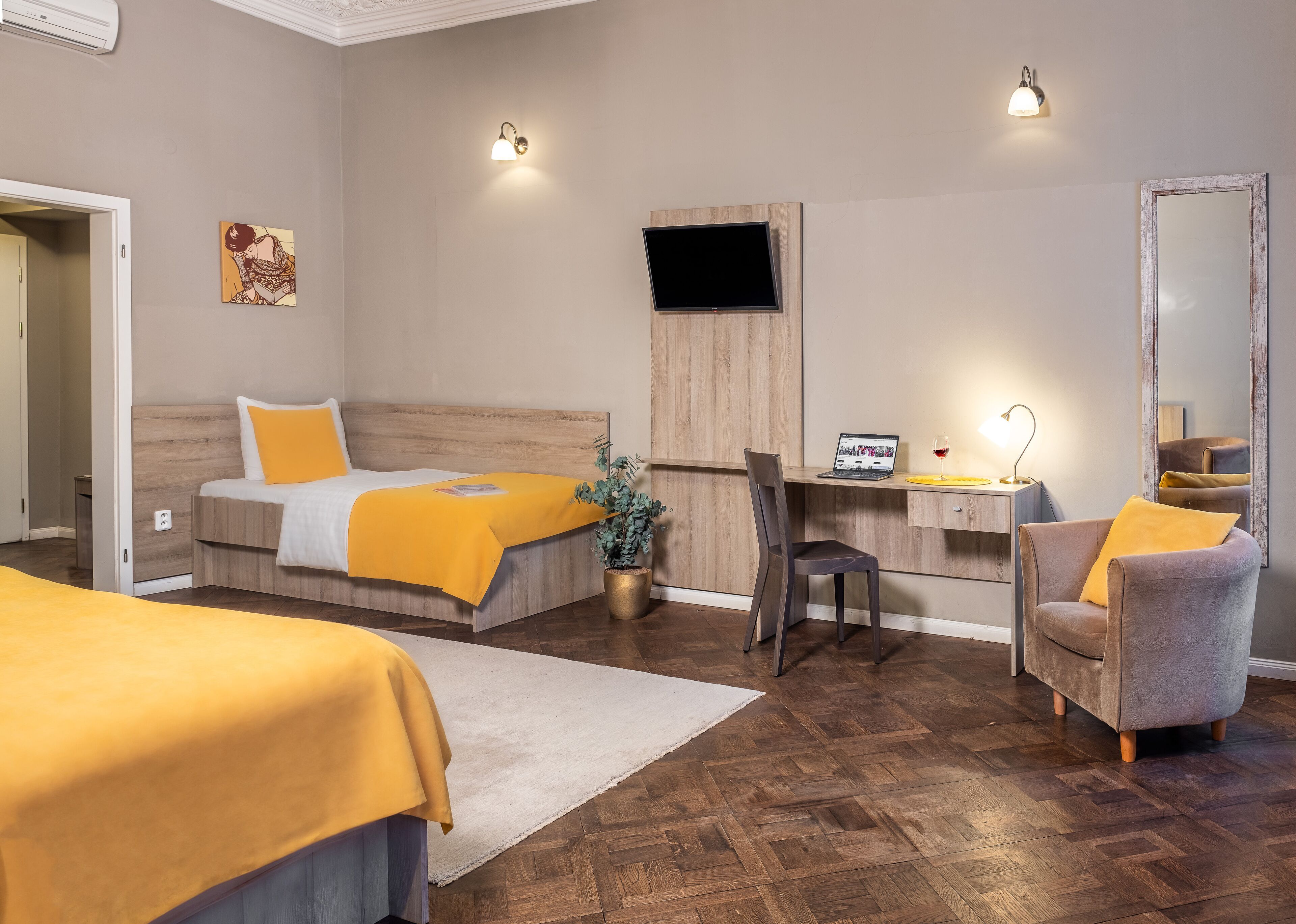 Habitación de hotel con dos camas, un escritorio con una computadora portátil, una silla, un espejo y una planta en maceta.
