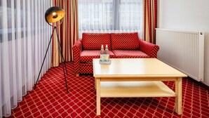 A room with a red patterned carpet, a red sofa with white polka dots, a wooden coffee table, a floor lamp, and a window with sheer curtains. -  Hotel Chateau Kurfürstendamm (Berlin)