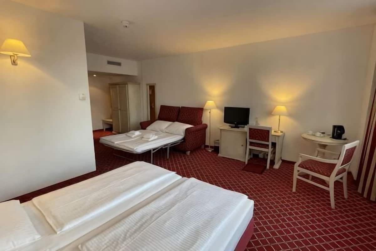 A hotel room with a bed, a desk with a chair, a television, and a small table with a chair.