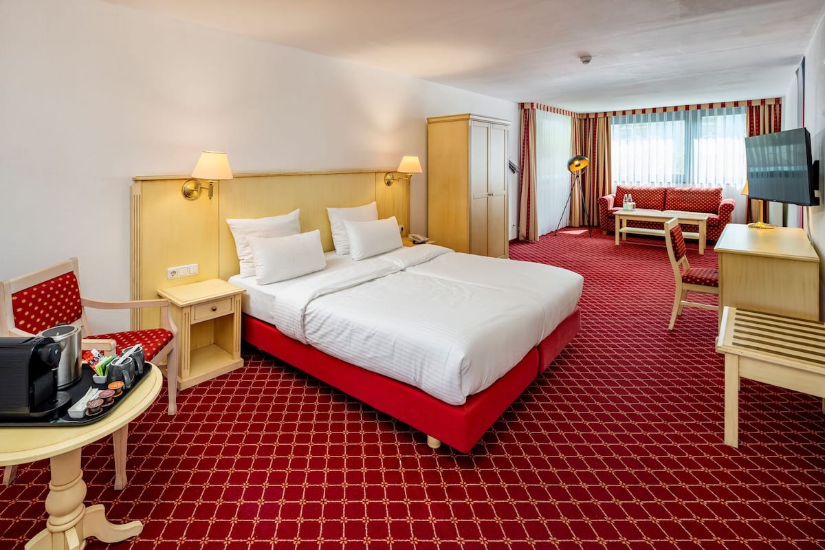 A hotel room with a large bed, a desk with a chair, a television, and a red carpeted floor.