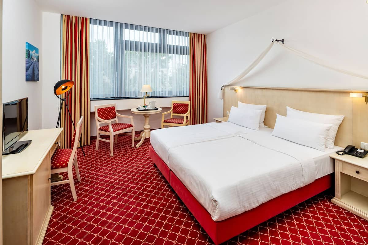 A hotel room with a bed, desk, chair, and a window with curtains.