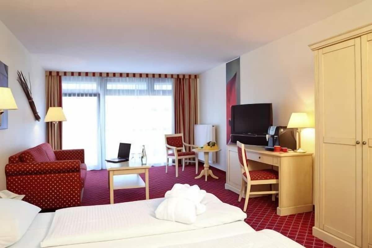 A hotel room with a bed, a desk with a computer, a TV, a chair, and a wardrobe.
