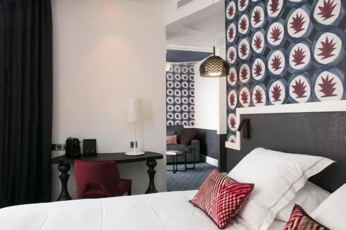 A hotel room with a bed, a desk, a chair, and a patterned wall.