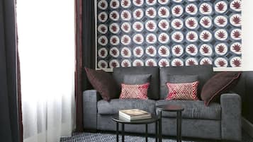 A modern living room with a grey sofa, patterned wallpaper, and a small round table.