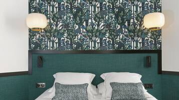 Une chambre d’hôtel avec un papier peint à motifs, un lit avec une literie blanche et des oreillers à motifs, deux lampes fixées au mur et une tête de lit recouverte d’un tissu vert.