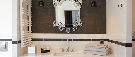 A modern bathroom with a white sink, two pendant lights, a decorative mirror, and a towel rack.