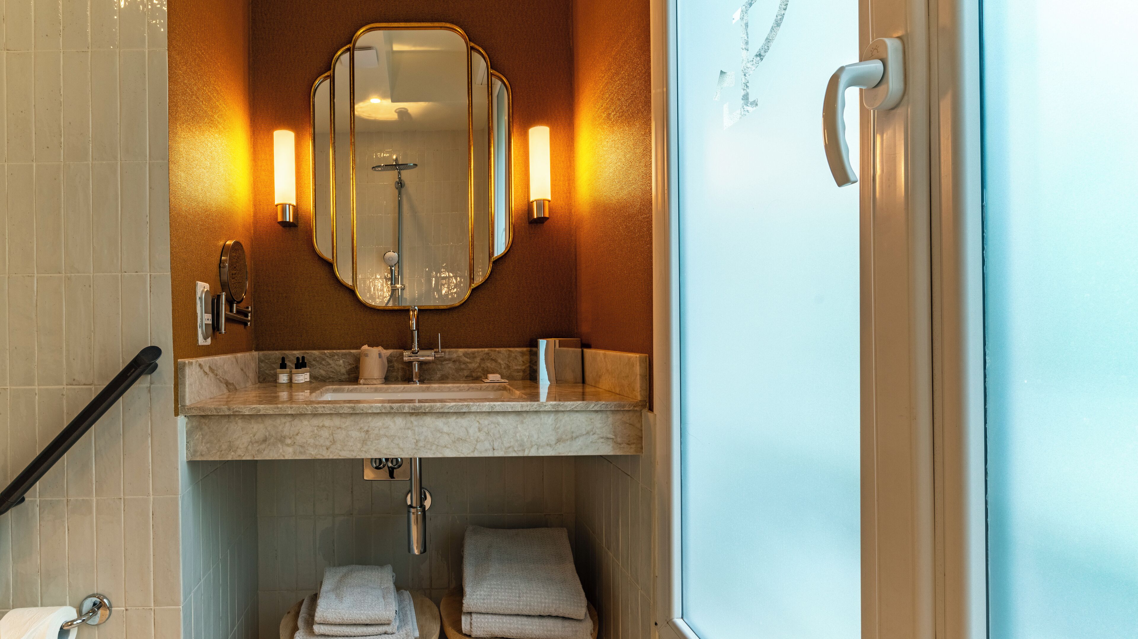 A bathroom with a marble sink, a large mirror, and two towels on the floor.