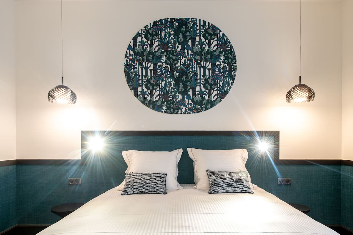 Un dormitorio con una cama grande, dos mesitas de noche, una obra de arte circular en la pared y dos lámparas colgantes.