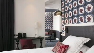 Habitación de hotel con cama, escritorio y silla. Pared con diseño y lámpara colgante.
