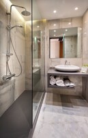 Un baño moderno con ducha de vidrio, suelo de mármol, lavamanos blanco y espejo sobre el lavamanos.