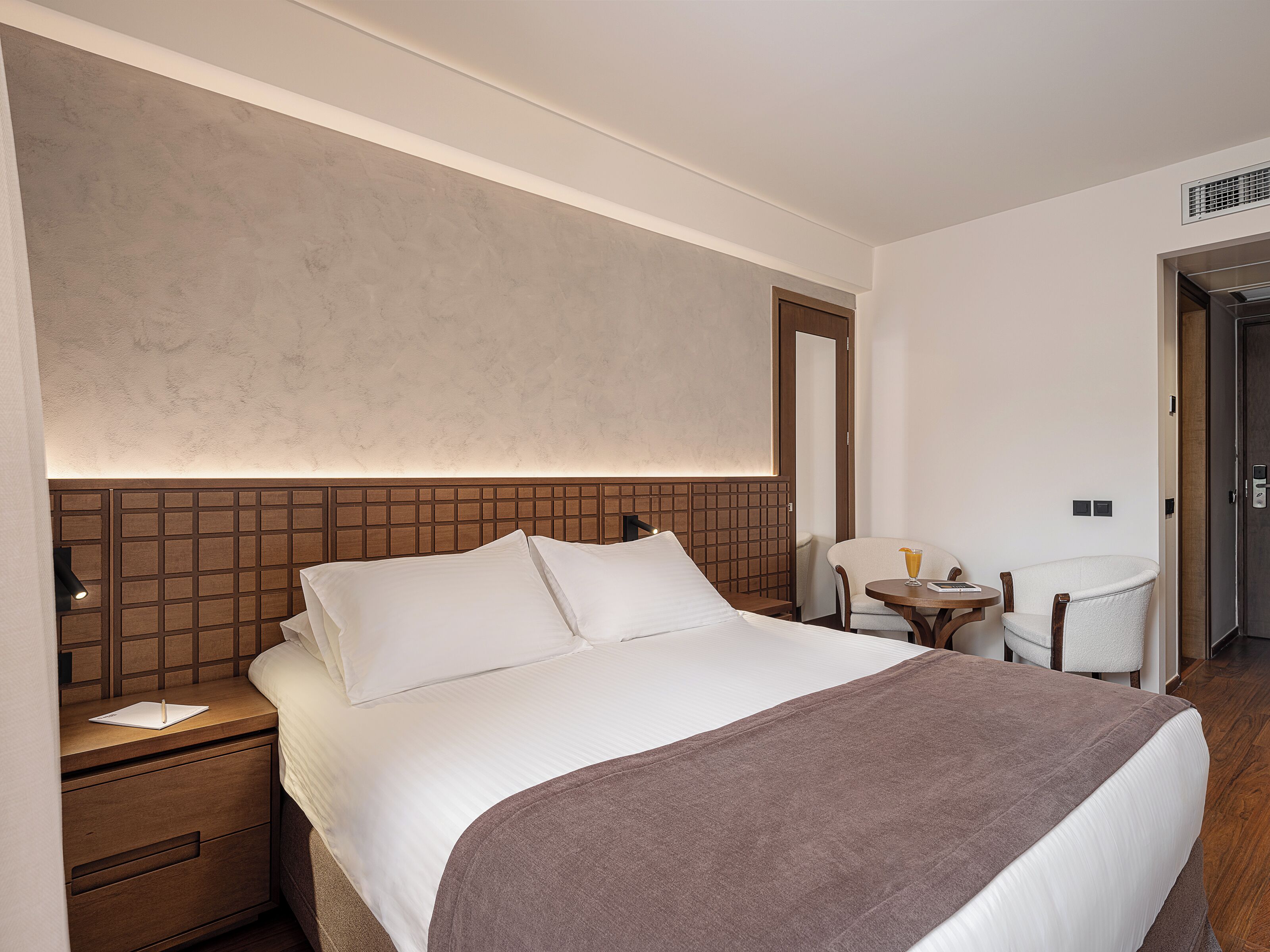 Una habitación de hotel con una cama grande, una mesita de noche, una silla y una pequeña mesa con una bebida.