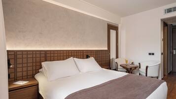 Una habitación de hotel con una cama grande, una mesita de noche, una silla y una pequeña mesa con una bebida.