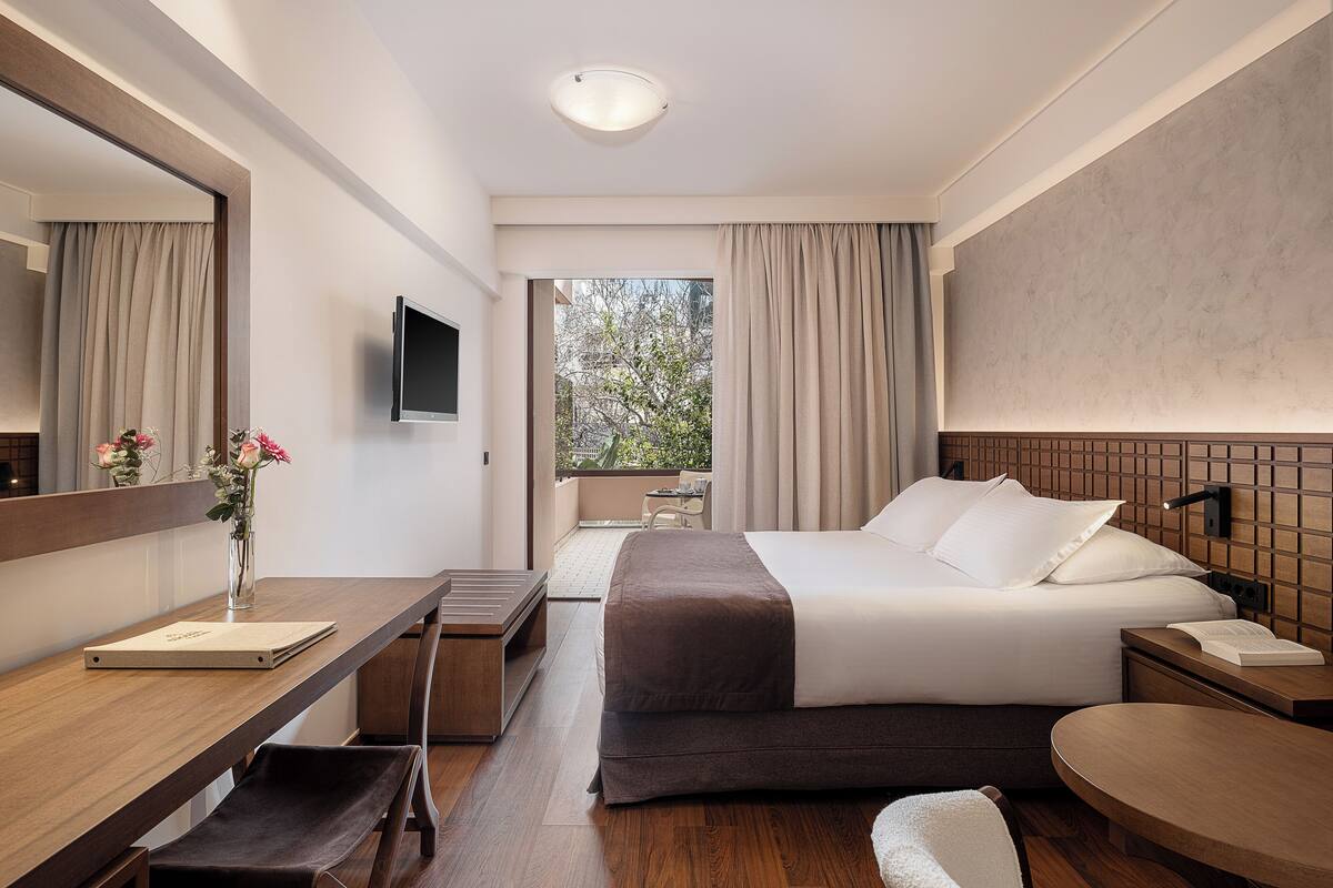 Ein modernes Hotelzimmer mit Bett, Schreibtisch, Stuhl und einem großen Spiegel.