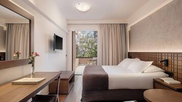 Quarto de hotel moderno com cama, escrivaninha, cadeira e um espelho grande.