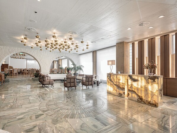 A spacious lobby with a marble floor, a reception desk, seating area, and a large arched doorway leading to another room. - Civitel Akali Hotel (Chania)