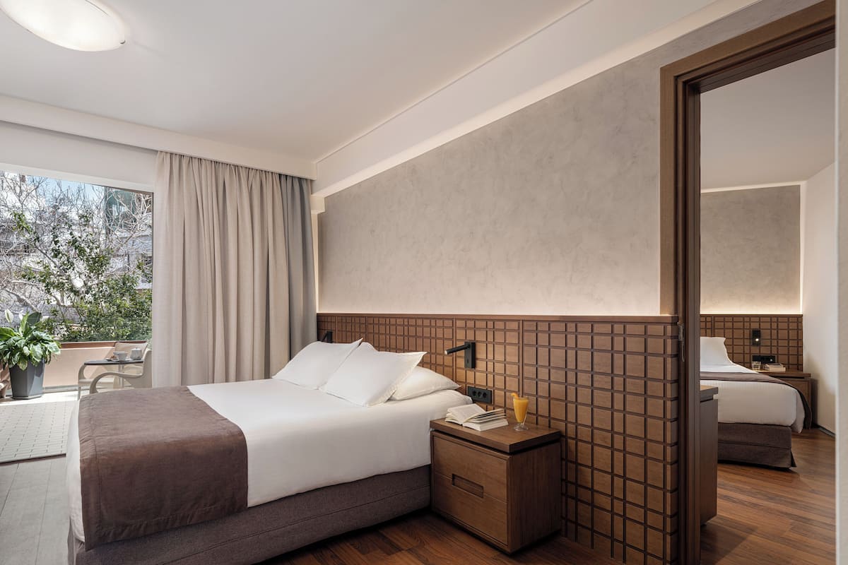 Ein modernes Hotelzimmer mit einem großen Bett, einem Nachttisch aus Holz, einer Nachttischlampe und Blick ins Freie.