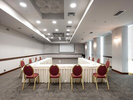 Μια αίθουσα συνεδριάσεων με ένα μεγάλο τραπέζι, κόκκινες καρέκλες και μια οθόνη προβολέα.