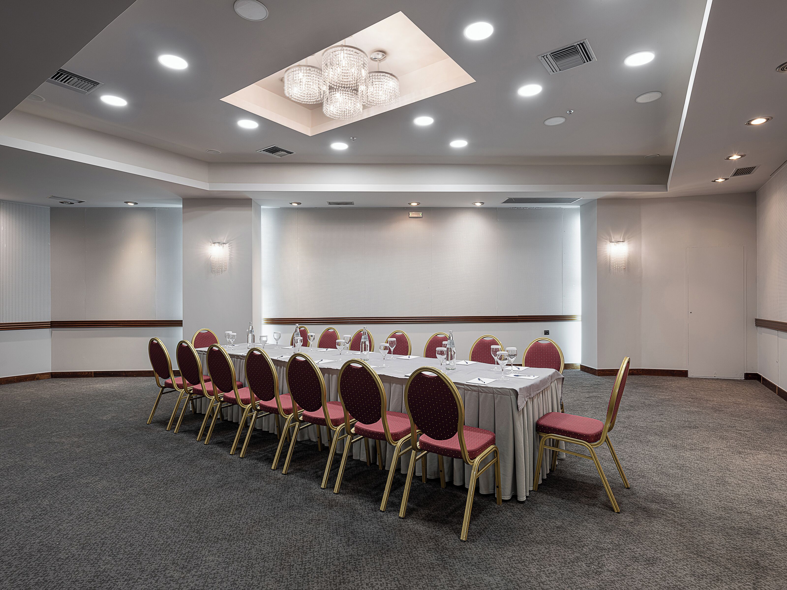 Un salón de conferencias con una larga mesa, sillas rojas y una araña de cristal.