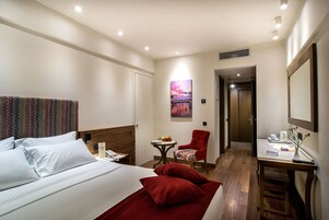 A hotel room with a bed, a desk, a chair, and a small table with a fruit bowl.